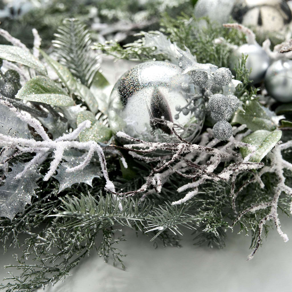 Decorative wreath with frosted branches and silver ornaments on a white background