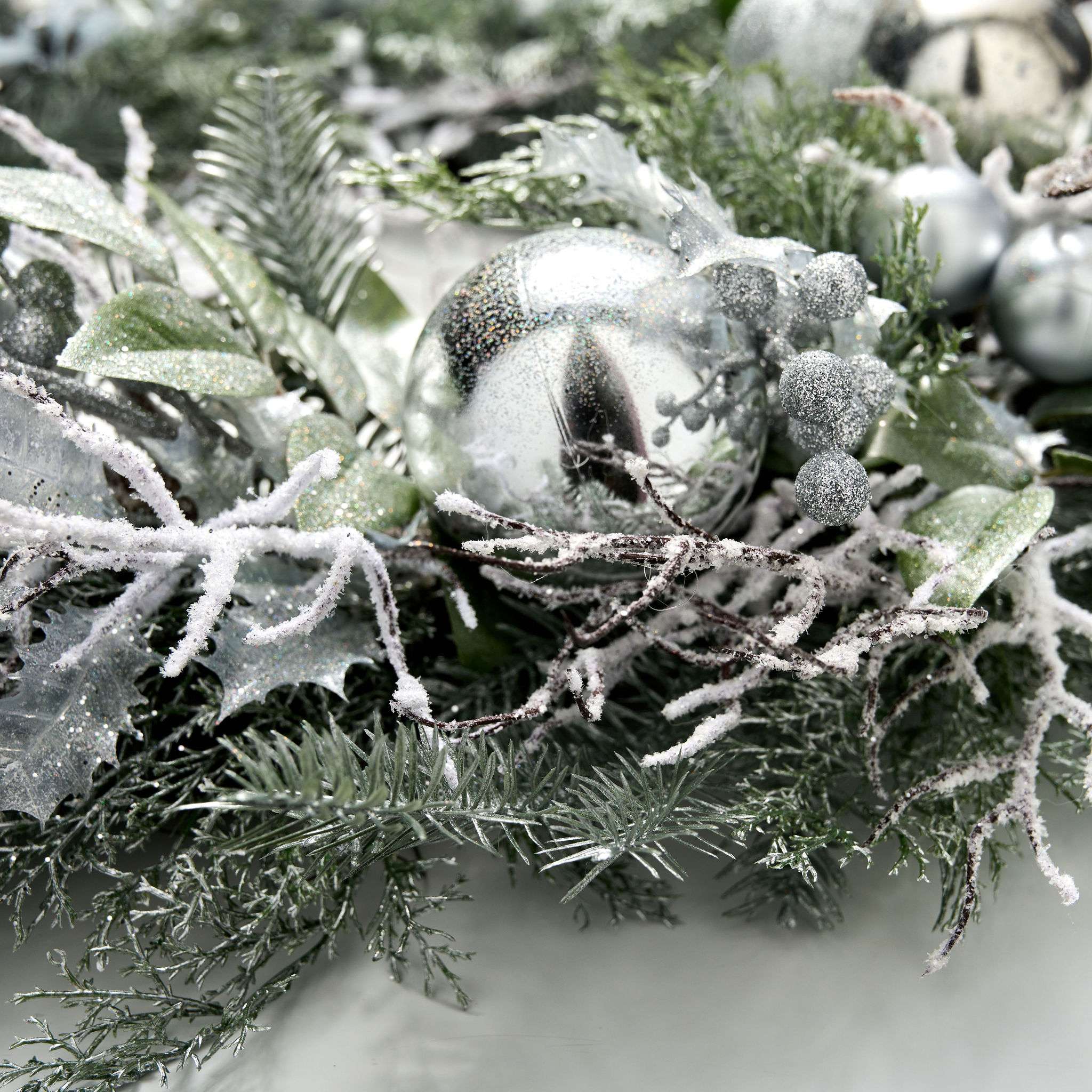 Decorative wreath with frosted branches and silver ornaments on a white background
