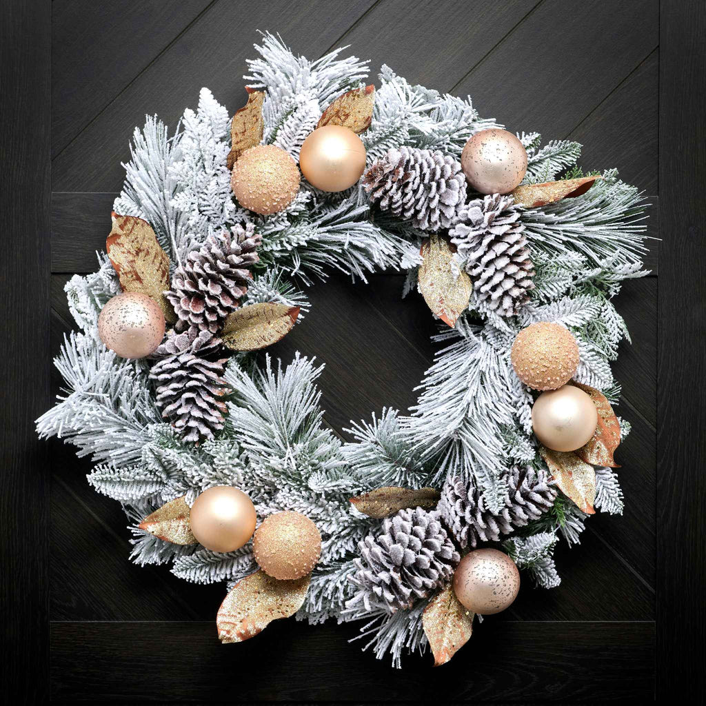 Decorative Christmas wreath with frosted pine branches, pinecones, and gold ornaments on a dark background.